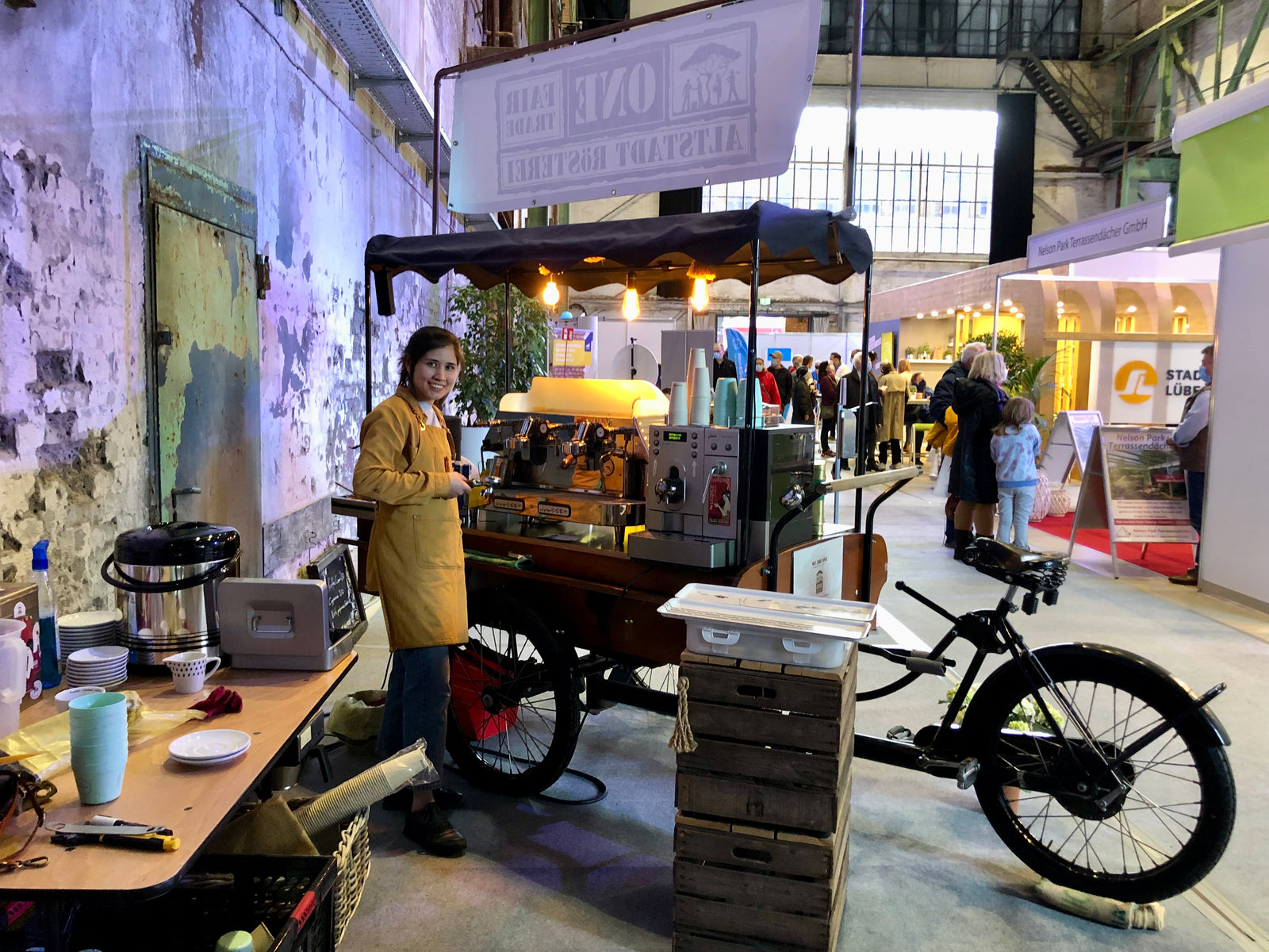 Coffee-Bike von ONE Fairtrade bei Indoor-Veranstaltung, Mitarbeiterin als Barista serviert frisch zubereitete Fairtrade Bio Kaffeespezialitäten