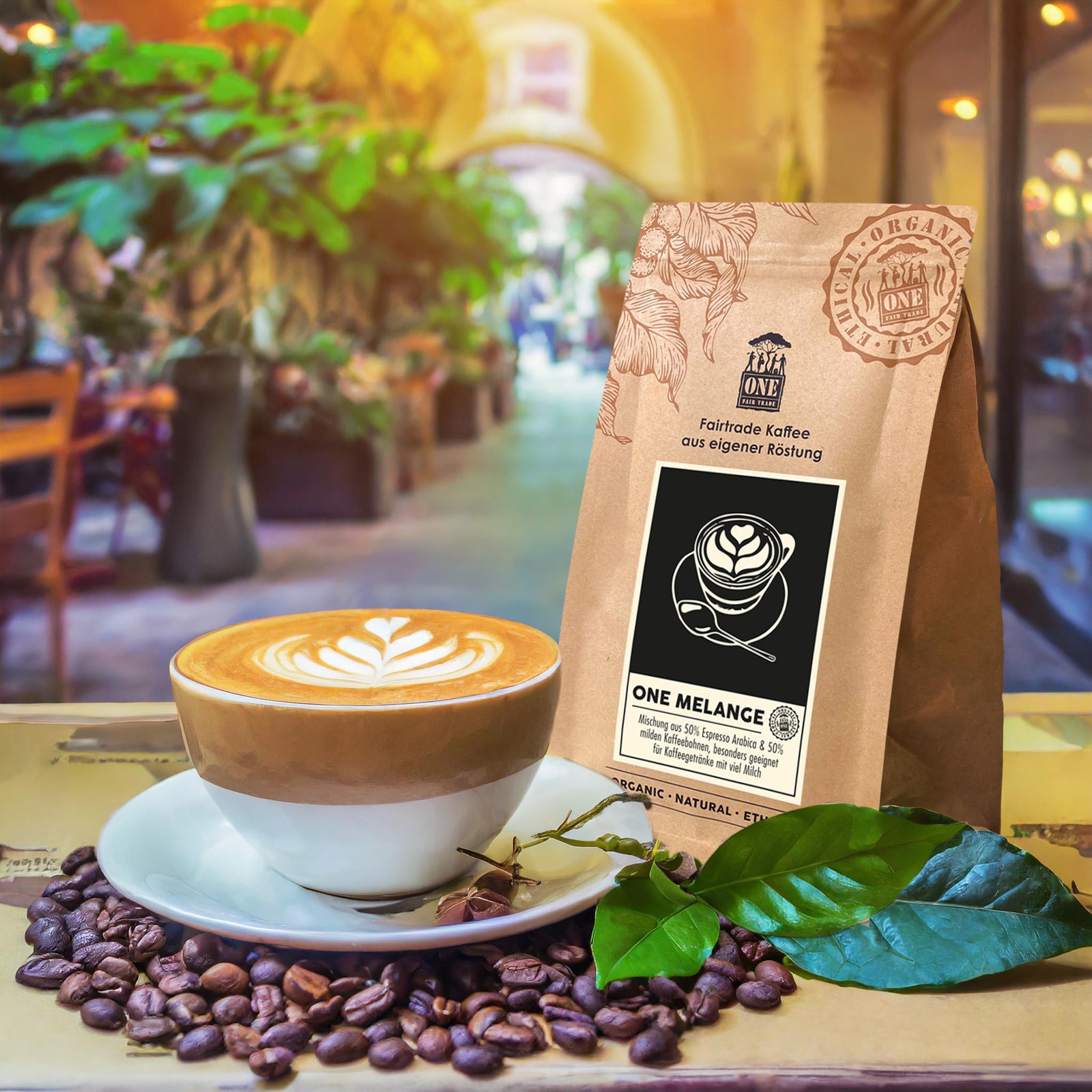 ONE Melange Tüte mit fairtrade Espresso-/Kaffeebohnen Mischung und Flatwhite als Dekoration. Der Hintergrund ist ein verschwommenes Café im Freien.