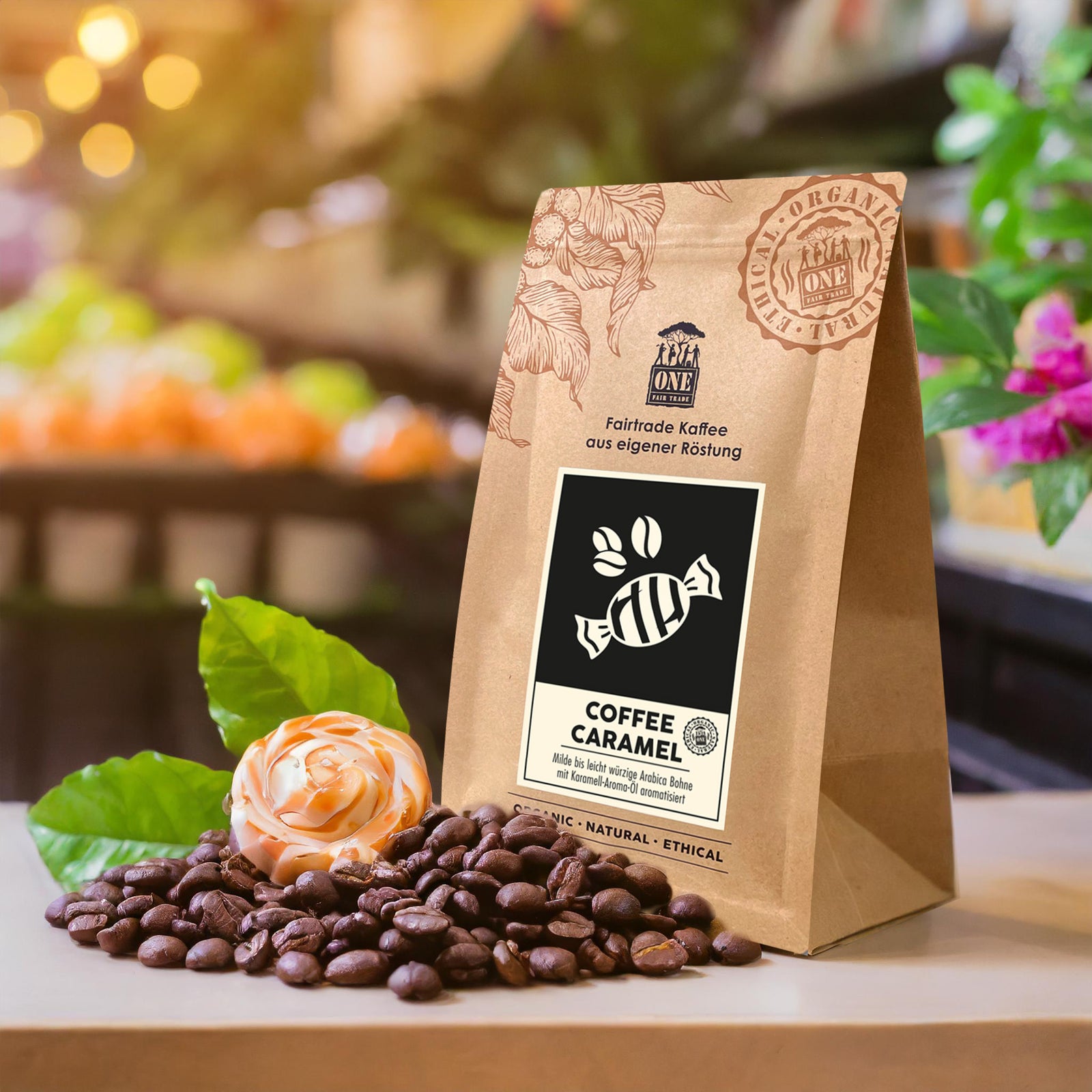 Coffee Caramel Tüte mit fairtrade Kaffeebohnen und Blume als Dekoration. Der Hintergrund sind verschwommene helle Farben.